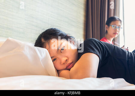 Zwei asiatischen Teenager im Schlafzimmer, einer Schwester im Bett und die andere Schwester sitzt am Fenster, in Konflikt Stellungnahme, gut für die Familie oder growin Stockfoto