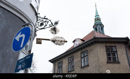 Schild zum Aufhängen des Schlosser im lateinischen Kopenhagen, Dänemark mit dem Turm der Sankt Petri Kirche im Hintergrund. Stockfoto