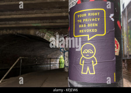 Street-Art-Poster hing an einer Säule in der Nähe eines Tunnels des Künstlers SUBDUDE mit stilisiertem Mann und Zeichentrick mit dem Slogan „Ihr Recht auf Privatsphäre wurde aufgehoben“. Stockfoto