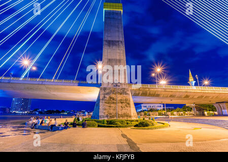 Rama-VIII-Brücke und Riverside Park bei Nacht in Bangkok. Stockfoto