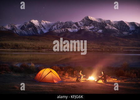 Zwei Männer, die Touristen an der beleuchteten Zelt in der Nähe von Lagerfeuer sitzen Stockfoto