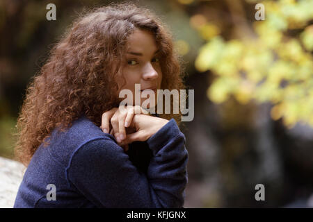 Ein unverfälschtes natürliches Porträt einer jungen Frau mit langen braunen Haaren und einem süßen, lächelnden Gesichtsausdruck in der herbstlichen Naturlandschaft Stockfoto
