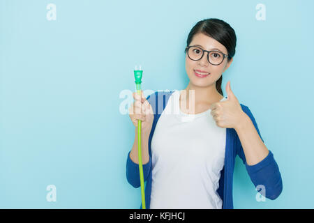 Schöne hübsche Dame Daumen oben Geste auf Kamera in blauen Hintergrund und Holding plug Linie Ausrüstung. Stockfoto