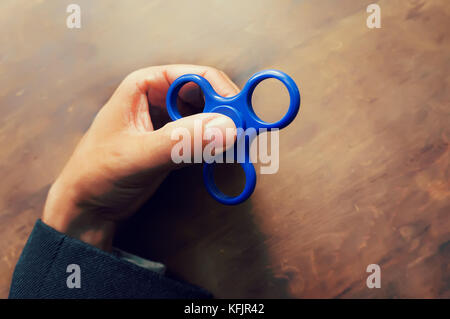 Ein Mann hand Halten einer Hand Spinner oder zappeln Spinner auf dem Hintergrund der hölzernen Tisch. Leistungsstarke Spinner, Twister für Hände Unterhaltung rotierende Spielzeug. Stockfoto