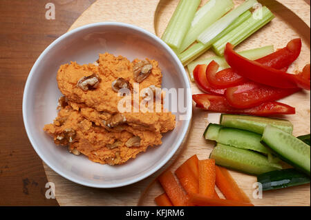 Frische hausgemachte Hummus mit Walnuss Stücke zusammen mit frisch geschnittenen Gemüse klebt auf einem hölzernen Platte Stockfoto