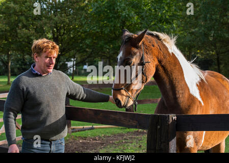 Mann mit Pinto Pferd/Quarter horse Hengst draußen im Feld innerhalb Holzgehäuse Stockfoto