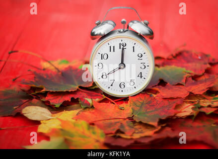 Alte Metall Wecker steht auf einer roten hölzernen Tisch unter den gefallenen Blätter im Herbst ein sonnigen Herbst morgen Stockfoto