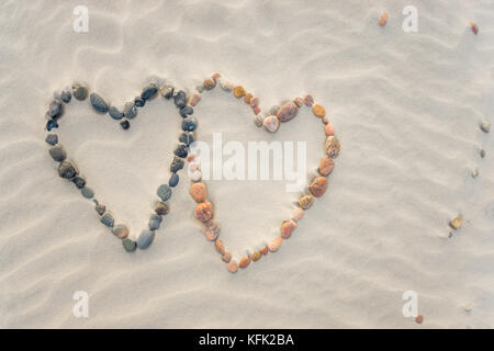 Pebbles angeordnet in Form von zwei Herzen auf Sand strand Wellen Stockfoto