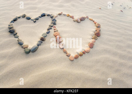 Pebbles angeordnet in Form von zwei Herzen auf Sand strand Wellen Stockfoto