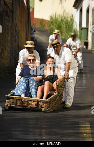 Madeira, Portugal - September 2017: Touristen eine Fahrt bergab in einem traditionellen Weidenkorb Rodelbahn genießen Stockfoto