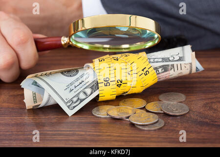 Bild der Geschäftsmann Prüfung der Banknoten und Münzen mit Lupe auf Tabelle abgeschnitten Stockfoto