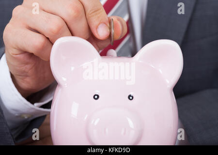 Bild der Geschäftsmann einfügen Münze im Sparschwein beschnitten Stockfoto