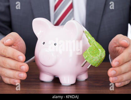 Mittelteil des Kaufmanns Abschirmung Sparschwein und grün Netzkabel am Schreibtisch Stockfoto