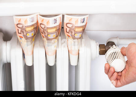 Euro-Banknoten in Heizkörper mit Thermostat einstellen Mann stecken Stockfoto