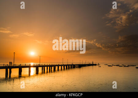 Sonnenuntergang in Alcochete, mit einem Pier bis zum Horizont. Silhouetten von zwei Menschen reden. Stockfoto