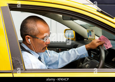 Ein thailändischer Taxifahrer raucht und nimmt sich einen Moment im Verkehr Zeit, um sein Telefon zu überprüfen. Stockfoto