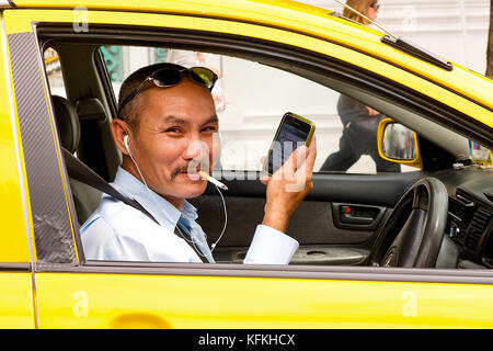 Eine thailändische Taxifahrer raucht und dauert einen Moment im Verkehr sein Telefon zu überprüfen. Stockfoto