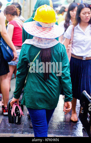 Eine thailändische Frau Bauarbeiter macht den Weg durch die Menschenmassen in einem belebten Markt Straße in Bangkok, Thailand. Stockfoto