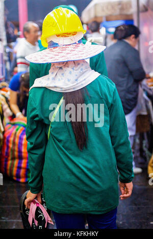 Eine thailändische Frau Bauarbeiter macht den Weg durch die Menschenmassen in einem belebten Markt Straße in Bangkok, Thailand. Stockfoto