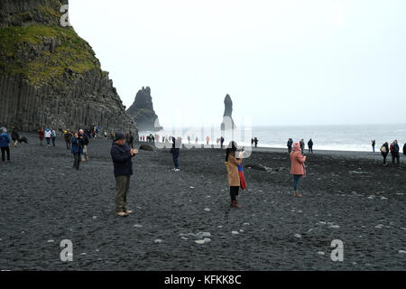 Reynisfjara schwarzer Sandstrand und Meer Stacks mit vielen Touristen fotografieren zeigt Stämme eines beliebten überfüllten Touristenziel, Vik, Island Stockfoto