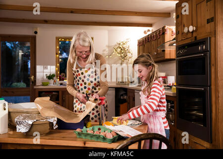 Kleine Mädchen Kuchen backen in der Küche mit ihrer Oma. Sie ist die Messung Zutaten, während die Großmutter Schnitte Backpapier. Stockfoto