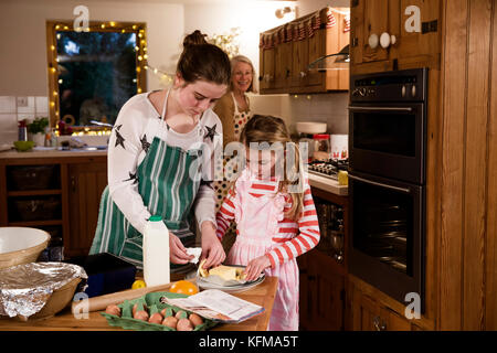 Zwei Schwestern sind Kuchen backen in der Küche mit ihrer Großmutter. Die Mädchen sind Messen, die Zutaten. Stockfoto
