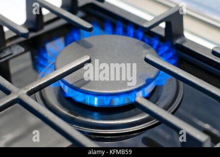 Gas Brenner brennt mit blauer Flamme auf dem Herd unter dem Schutzgitter. Foto mit geringer Tiefenschärfe. Stockfoto