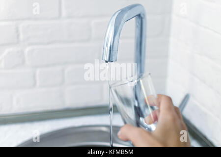 Women's Hand hebt das Glas mit dem Wasserstrahl aus dem Wasserhahn. Platz für Text. Foto mit heiligen Tiefenschärfe. Stockfoto