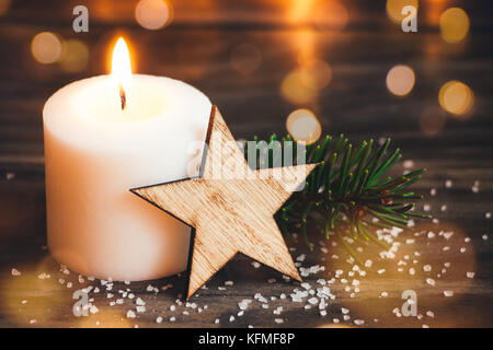 Weihnachten weiße Kerze mit einem hölzernen Stern, tanne Zweig und Lichter Bokeh im Hintergrund Stockfoto