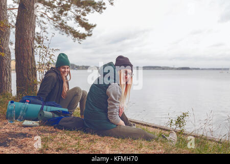 Lächelnde junge Frauen ruht während der Reise in der Nähe des Sees. Stockfoto