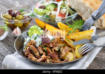 Griechische Schwein Gyros in eine eiserne Pfanne, serviert mit Tzatziki und Bratkartoffeln, pitabread, Salat und Oliven Stockfoto