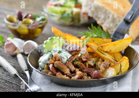 Griechische Schwein Gyros in eine eiserne Pfanne, serviert mit Tzatziki und Bratkartoffeln, pitabread, Salat und Oliven Stockfoto