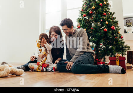 Kleine Familie glücklich zusammen Zeit haben zu Weihnachten. Junges Paar mit Kind sitzen neben dem Weihnachtsbaum Geschenke öffnen. Stockfoto