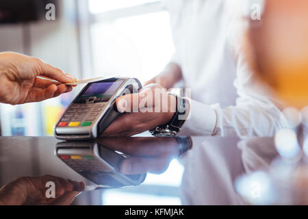 Hand des Kunden bezahlen mit kontaktlosen Kreditkarte mit der NFC-Technologie. Bartender mit einem credit card reader Maschine an der Theke mit weiblichen holdi Stockfoto