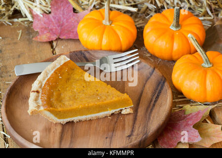 Slce von Pumpkin Pie auf einer Holzplatte mit Kürbissen Stockfoto