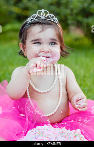 Smiling Happy Baby Kleinkind Mädchen feiern ersten Geburtstag Jahrestag Partei. Holding und kauen Kerze mit schmutzigem Gesicht von rosa Kuchen, was für ein Chaos Stockfoto