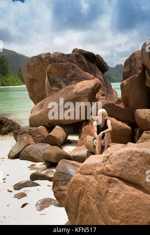 Die Seychellen, Praslin, Anse Volbert, Cote d'Or Strand Frau auf den Felsen zu sitzen atat Anse Regierung Stockfoto