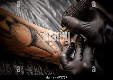 Ein professionelles Tattoo Künstler stellt schwarze Tinte in die Haut mit einer Nadel von einem Tattoo Maschine. Stockfoto