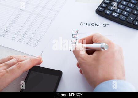 Nahaufnahme von Hand mit Stift über Antragsformular mit Handy und Rechner Stockfoto