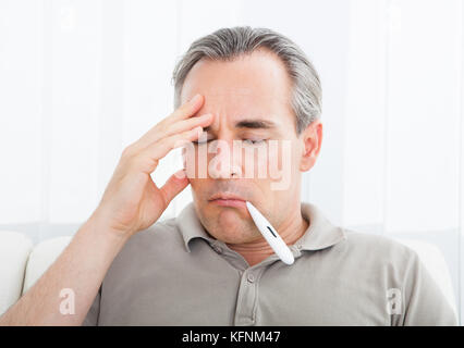 Porträt eines kranken Mannes mit Thermometer in den Mund Stockfoto