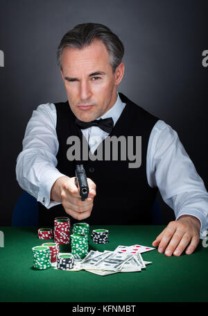 Croupier mit Stapel von Token-Chips und Banknote auf dem Tisch mit einem Gewehr zielen Stockfoto