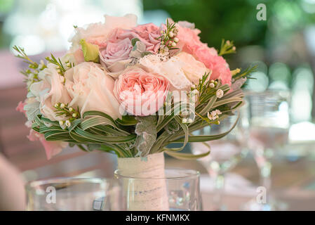 Runde Brautstrauß mit Pastellfarben, Pfingstrosen und Rosen, Spitze und Grün, in einem transparenten Vase set Stockfoto