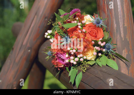 Orange Farbtöne wedding bouquet mit Freesien, Rosen und Beeren auf einem rustikalen hölzernen Zaun aufgestellt, die unter der Sonne Stockfoto