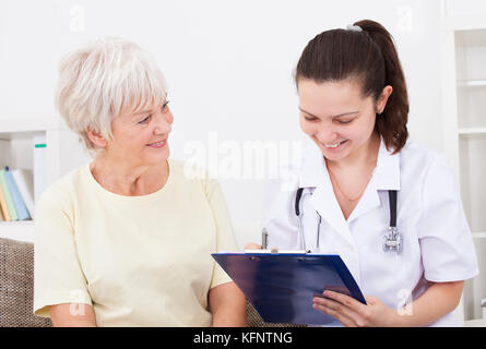 Junge weibliche Arzt schreiben auf Zwischenablage saß bei älteren Patienten Stockfoto