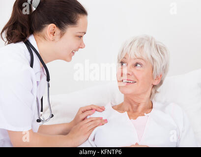 Glückliche junge Frau Doktor mit Hand auf älterer weiblicher Patient Stockfoto