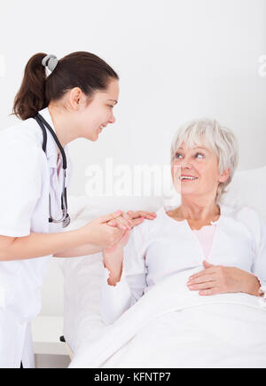 Glückliche junge Frau Doktor mit Hand auf älterer weiblicher Patient Stockfoto