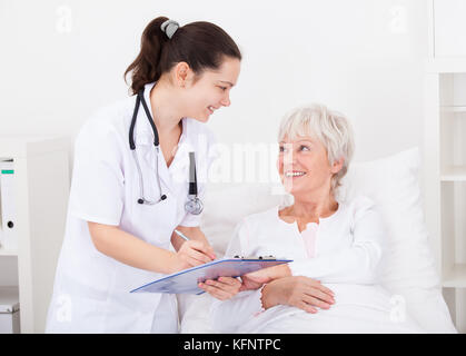 Senior weiblicher Patient, Arzt schriftlich über die Zwischenablage Stockfoto