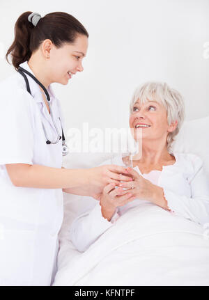 Junge weibliche Arzt, Glas Wasser zu den älteren weiblichen Patienten Stockfoto