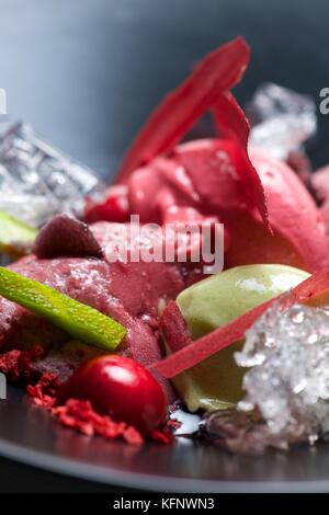 Erdbeeren und Pistazien Eis mit Kirschen in einem schwarzen Schüssel. Stockfoto