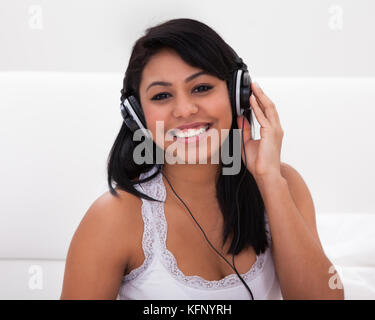 Junge Frau Hören von Musik über Kopfhörer beim liegen auf dem Bett Stockfoto